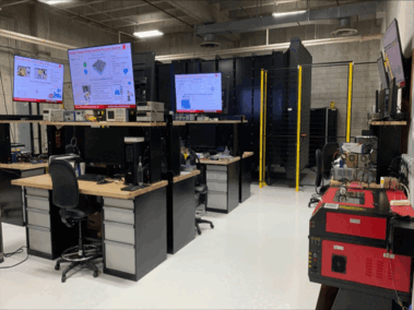 Modern electronics lab with workstations, screens, testing equipment, and organized tools.