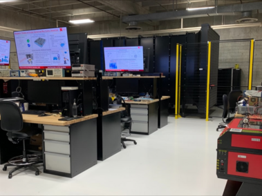 Workstations in a modern lab with screens, desks, and equipment on a white floor.