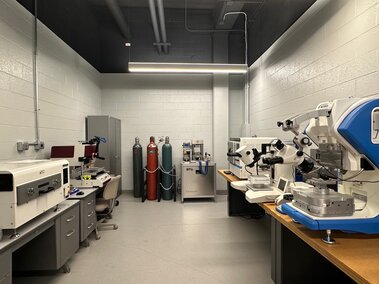 Laboratory with microscopes, desks, gas cylinders, and white walls under bright ceiling lights.